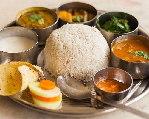 A round tray with rice, lentil soup, cooked vegetables, and pickles, a traditional Nepali dal bhat meal