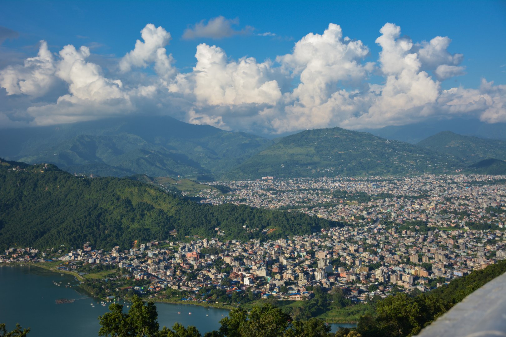 A wide view of Pokhara city with buildings, green hills, and snow-capped mountains in the background