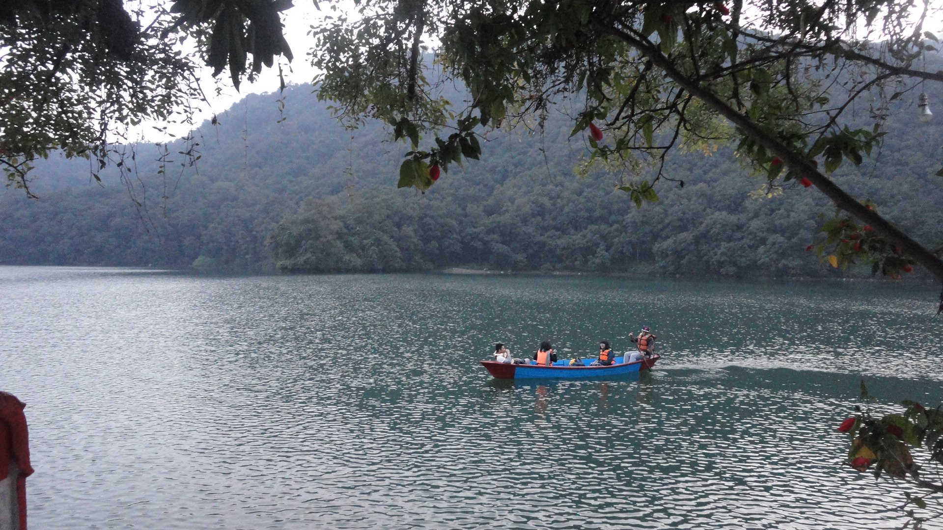 A wooden rowboat on the still blue water of Phewa Lake with mountains reflected in the water