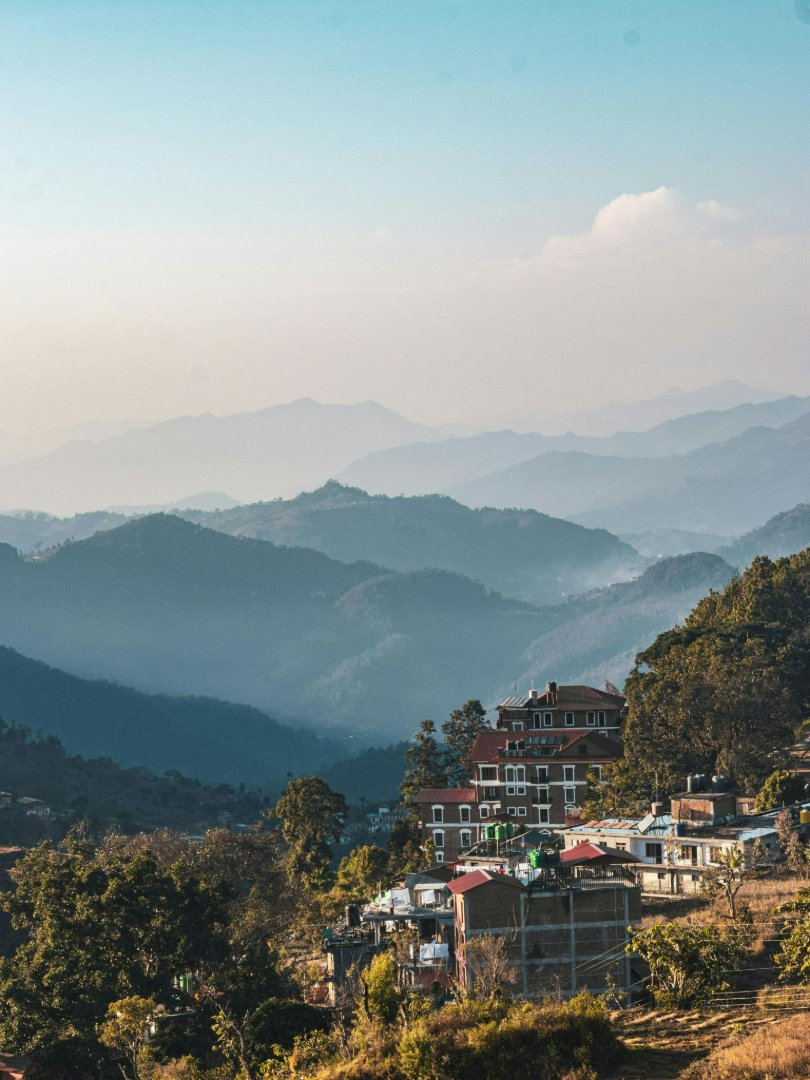 Nagarkot village buildings and hotels on hillside with layered blue mountain ridges in morning haze